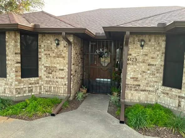 Brown seamless gutters and downspouts framing a buff-brick entryway